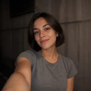 A woman taking an arm's-length selfie that stops at her waist, in a blurred concrete garage