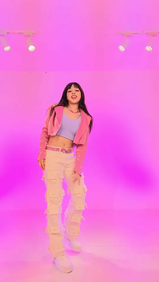 The dancer in magenta light smiling at the camera with her arms loose