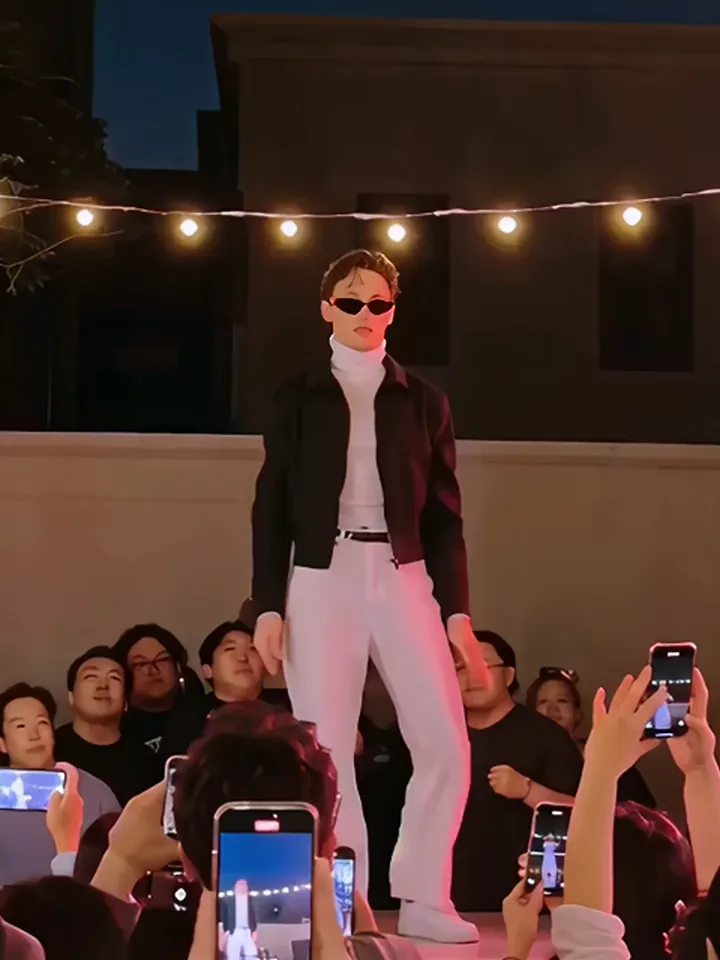 The dancer in sunglasses, a black jacket and white trousers standing ready on stage before the routine starts