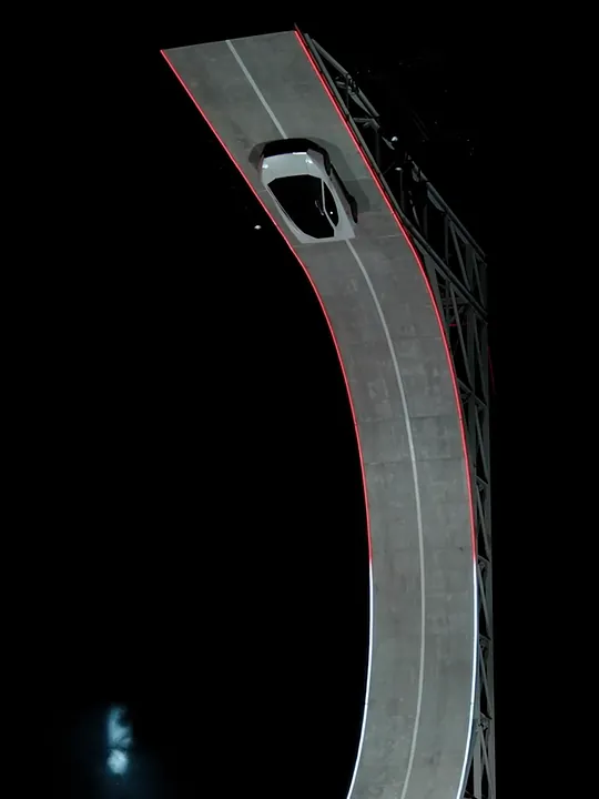 A car upside down near the top of a tall curved concrete ramp at night