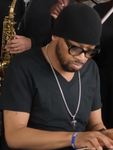 Keyboard player in a black beanie, glasses and a silver chain playing at the front