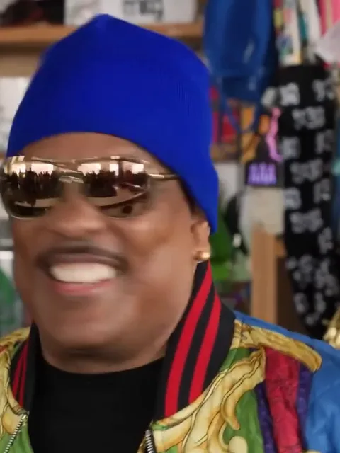 Close-up of the singer in the blue beanie and gold mirrored sunglasses, grinning