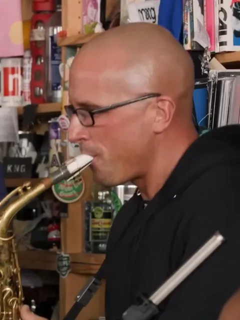 Sax player in glasses and a black hoodie playing side-on