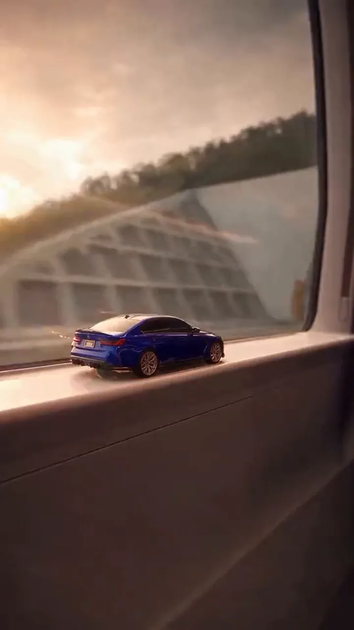 A tiny car sits on a train window ledge in sunset light, the window frame filling the picture