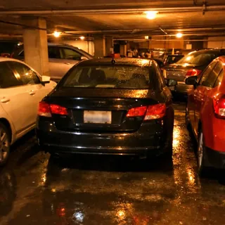 Several cars parked tightly in a dim car park at night, one of them in the middle of the row