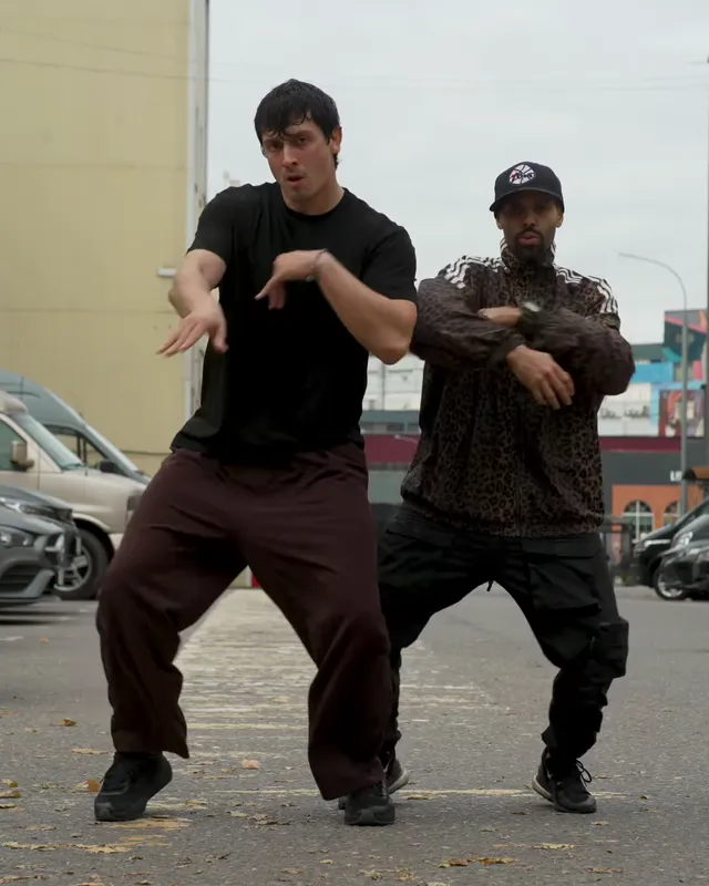 Both dancers stand wide with knees bent and forearms stacked across their chests