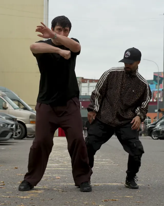 The left dancer crosses his hands in front of his face while the right one stays low beside him