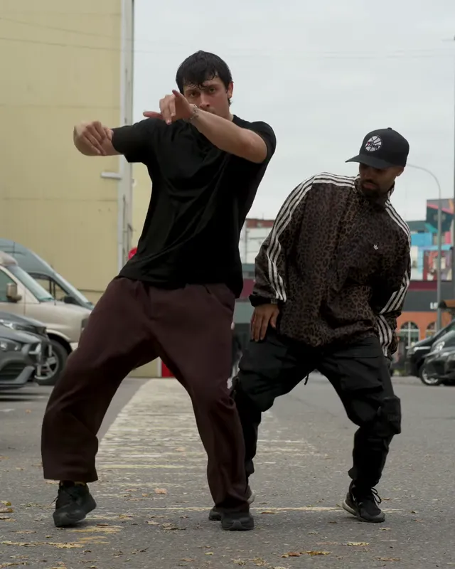The dancers sink into a low wide squat, the left one reaching an arm across his chest