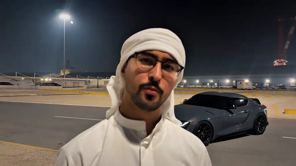 The man talks to the camera with a grey sports car now parked behind him