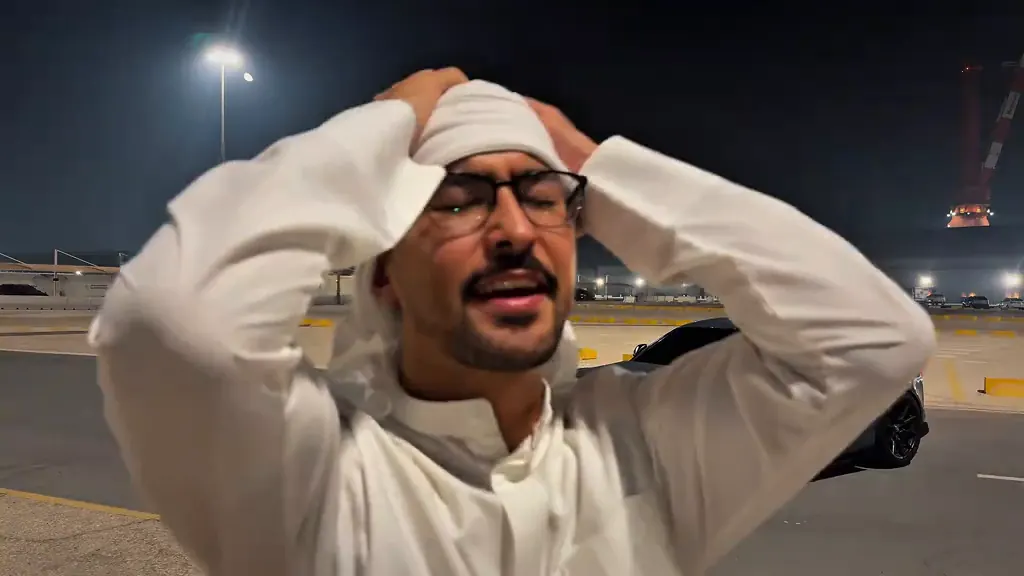 The man holds his head with both hands, the sports car behind him
