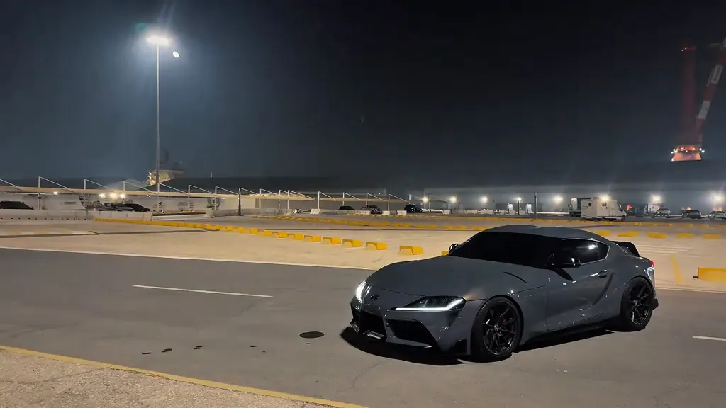 The grey sports car alone in the floodlit lot after the man walks out of frame